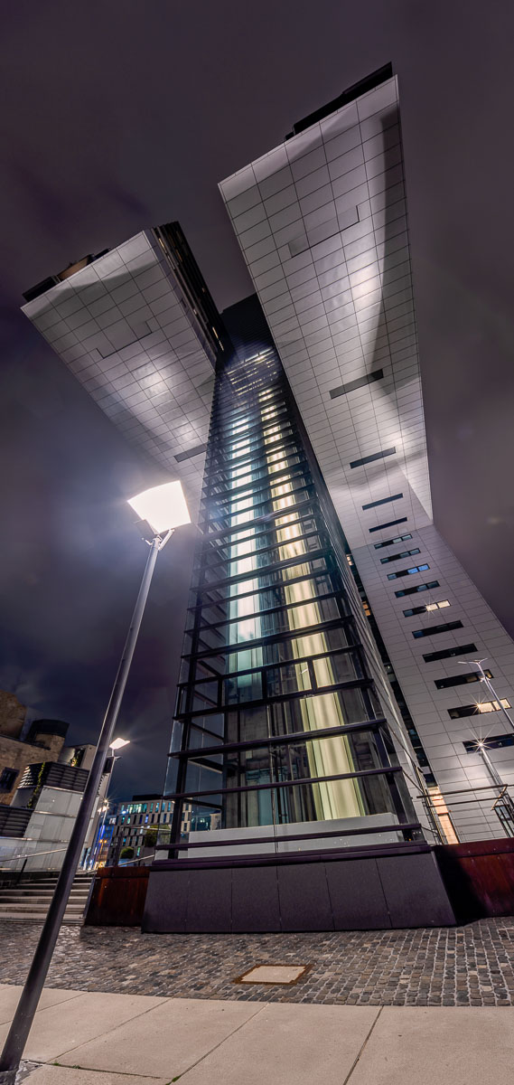 Dramatische Architekturaufnahme eines Kölner Kranhauses von unten mit beleuchteten Aufzügen als Lichtspuren